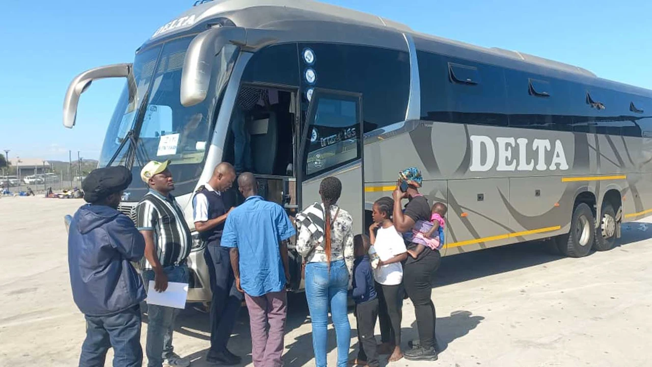 People wait in line to board a gray bus labeled "Delta" on a clear day. The scene conveys anticipation and travel.